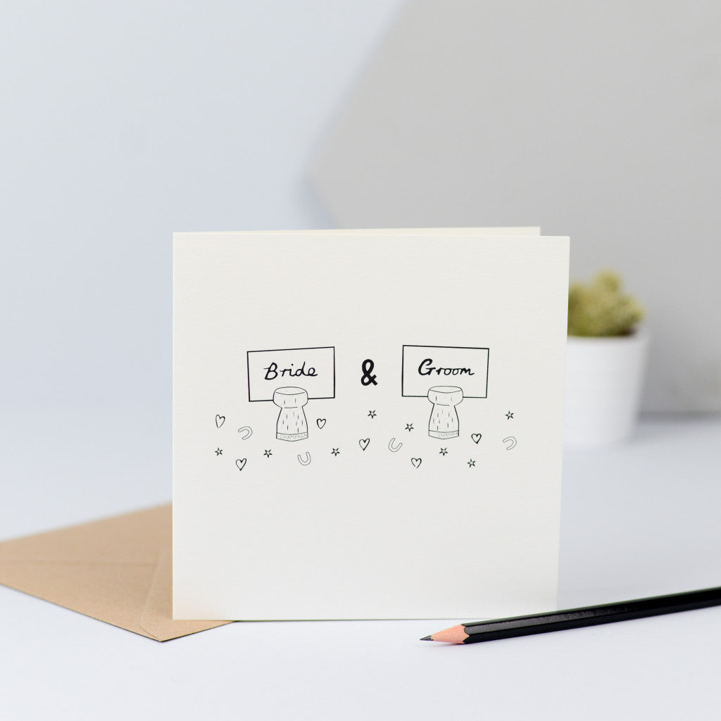 A sweet design with a hand drawn illustration of two champagne corks with the place names for the Bride and Groom stuck in them and surrounded by confetti.