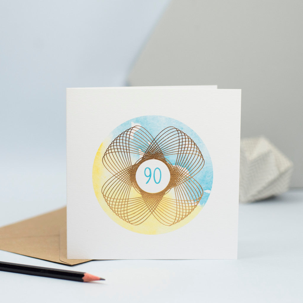 a unisex 90th birthday card with blue and yellow watercolour and a gold foil spirograph
