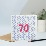 A 70th design created through mark making, with a blue dotty textured background and a maroon 70 in the foreground.