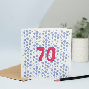 A 70th design created through mark making, with a blue dotty textured background and a maroon 70 in the foreground.