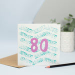 An 80th design created through mark making, with a green textured zig zags in the background and a pink 80 in the foreground.