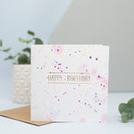 A pink and purple watercolour splattered background with gold foil happy birthday in the foreground