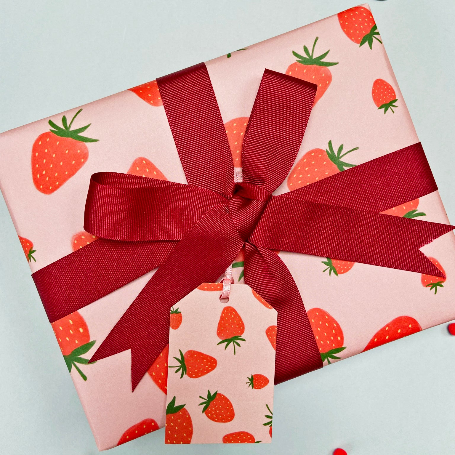strawberry wrapping paper with an maroon ribbon bow and matching gift tag